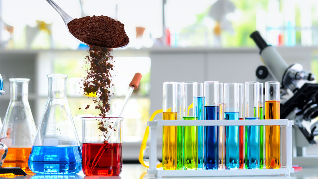 Pouring soil into a red liquid with colorful test tubes beside it.