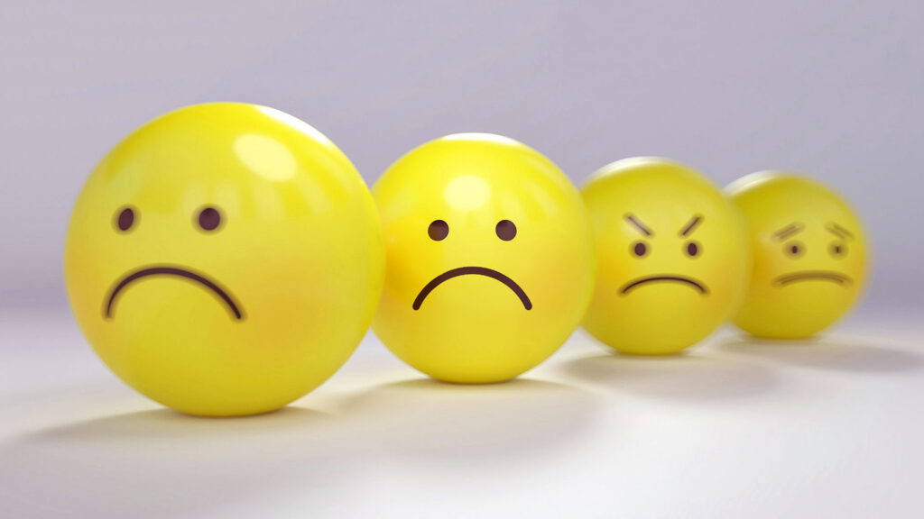 Three yellow balls with sad and angry faces on a gray background.