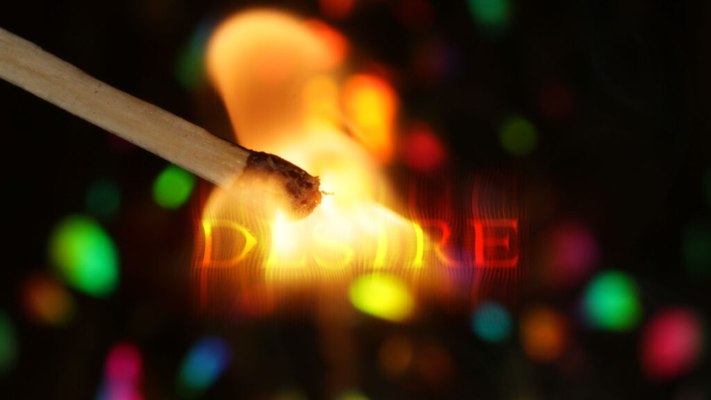 A lit match ignites the word 'DESIRE' glowing in warm light.