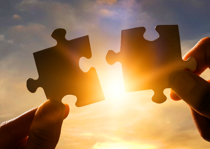Two puzzle pieces joining together against a glowing sunset.