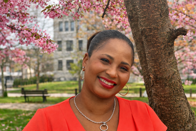 Woman smiling under blooming pink cherry blossoms.