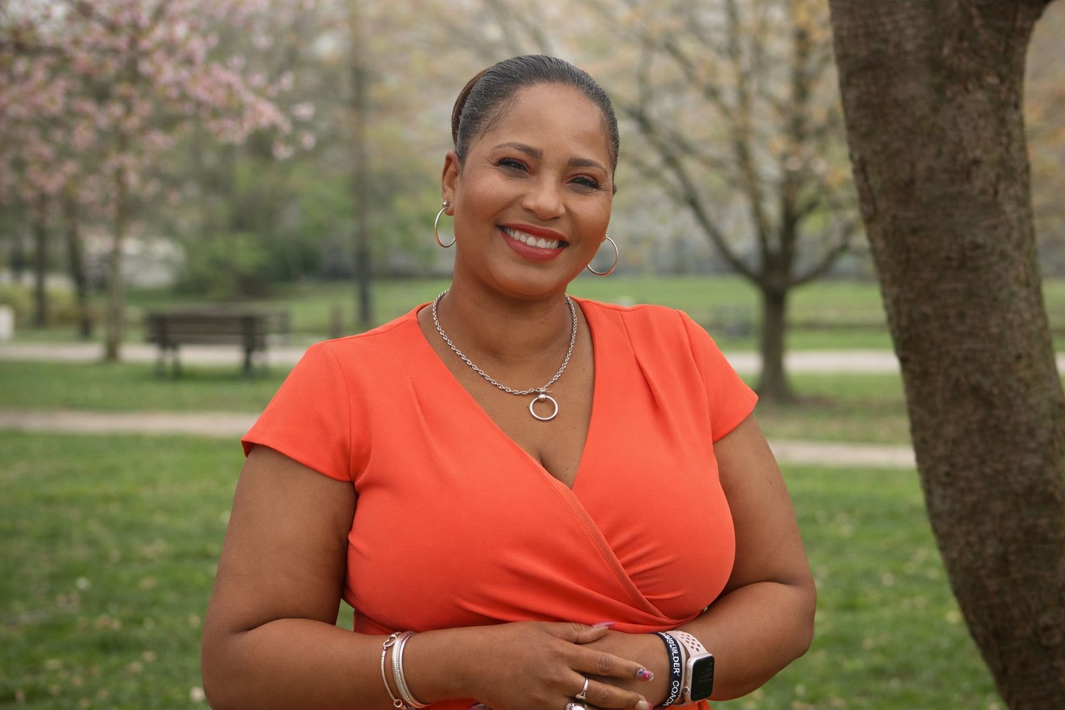 Woman smiling outdoors in an orange top.