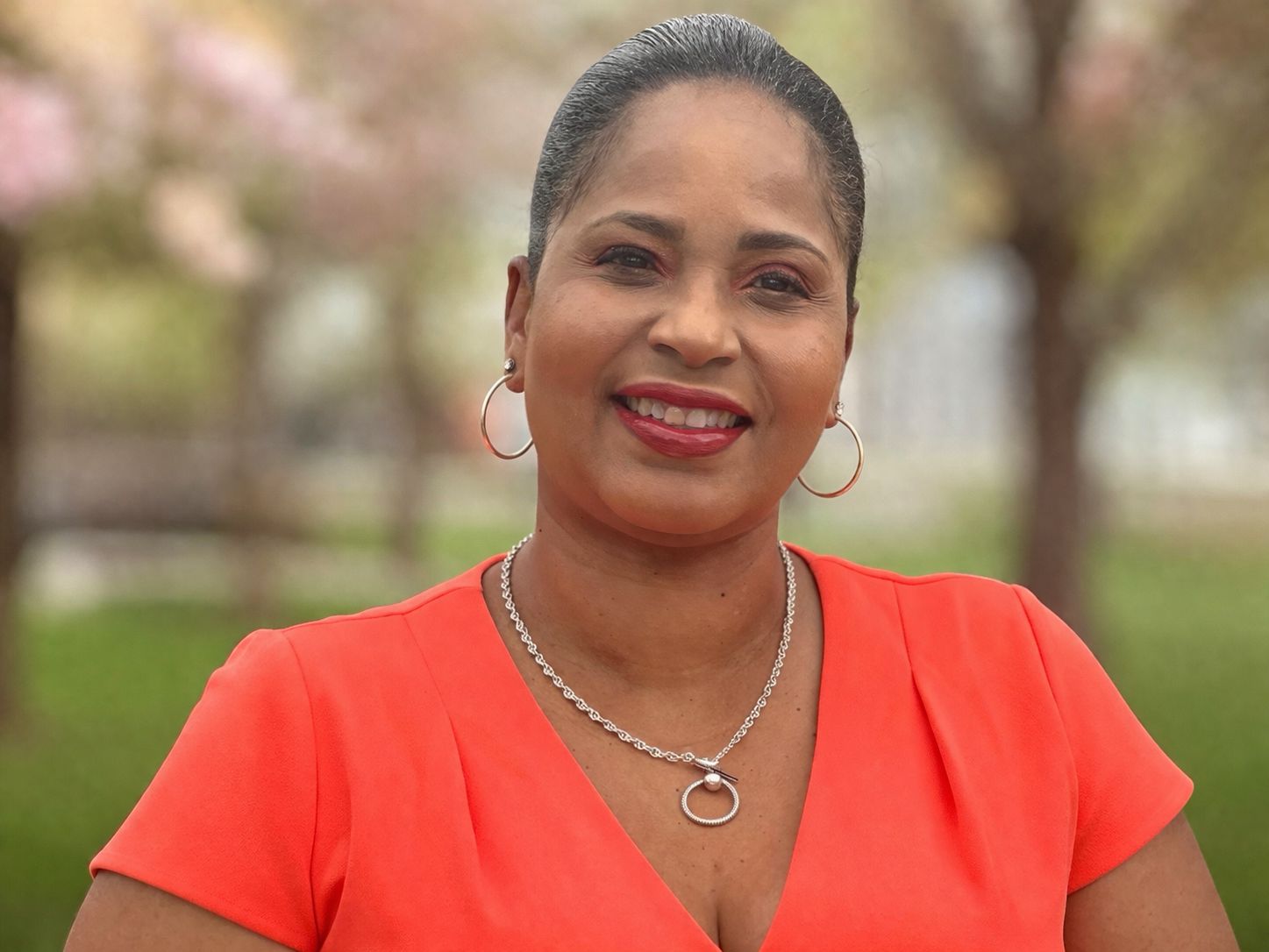 A smiling woman wearing a red top outdoors.